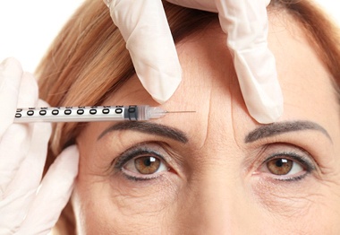 A dentist injecting Botox in Hoboken into the area between a woman’s eyebrows