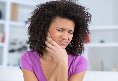 Woman in need of tooth extraction holding cheek in pain