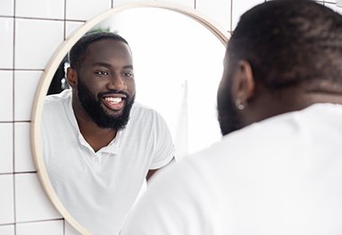 Man in white shirt checking his smile in the mirror