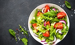 Plate with salad that includes leafy greens, tomatoes, and onions