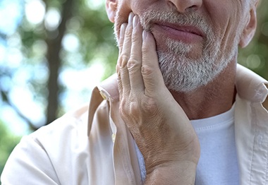 Closeup of man holding his right cheek because of a sensitive dental implant 
