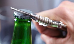 green glass bottle being opened with bottle opener 