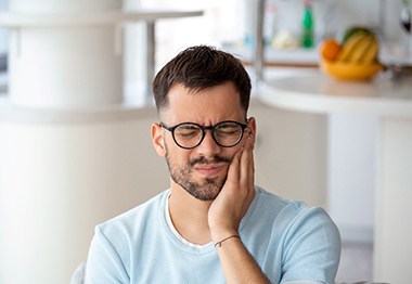 Closeup of man with glasses struggling with tooth pain