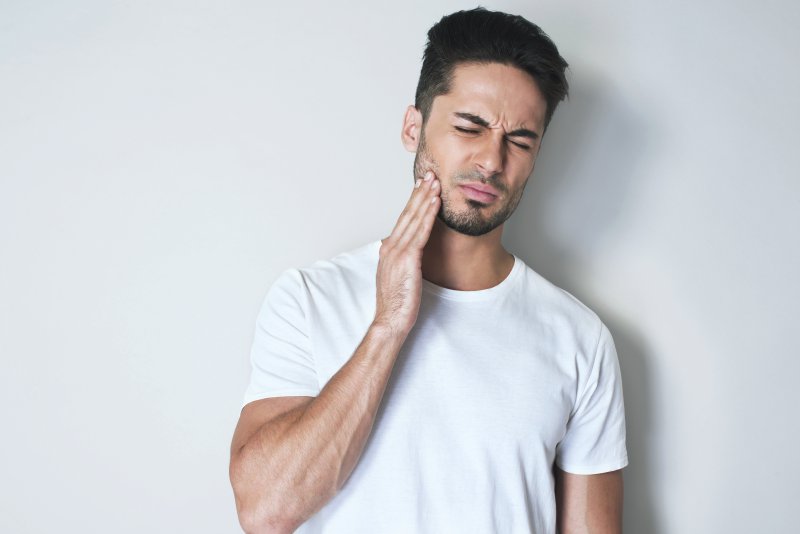 Man with a failed dental implant touching his cheek